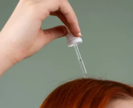 a dropper of hair serum held above red hair