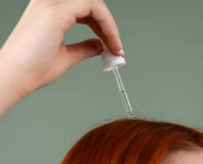a dropper of hair serum held above red hair