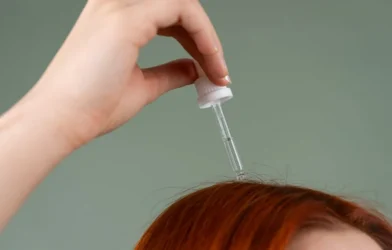 a dropper of hair serum held above red hair