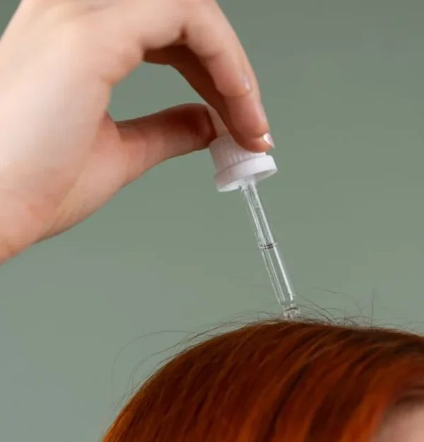 a dropper of hair serum held above red hair