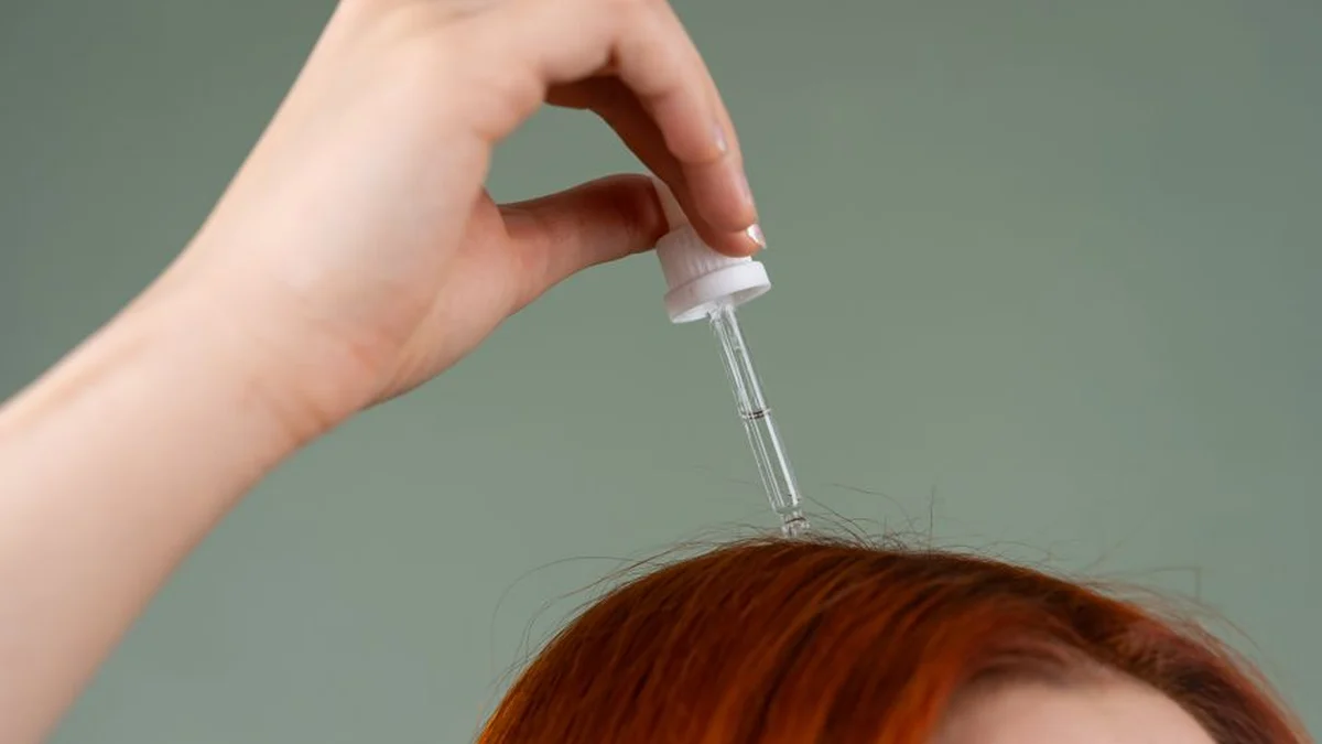 a dropper of hair serum held above red hair