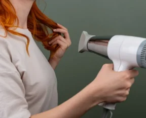 woman drying her hair with a white hair dryer at home