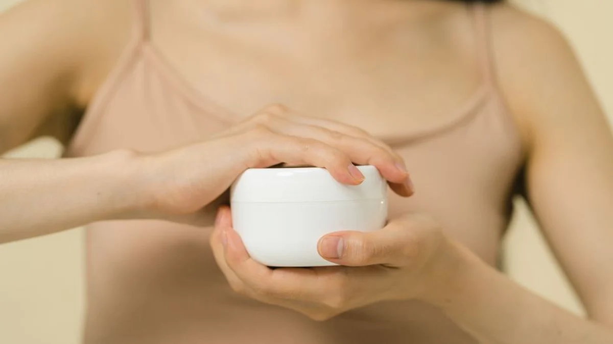two hands holding a white pot of hair cream