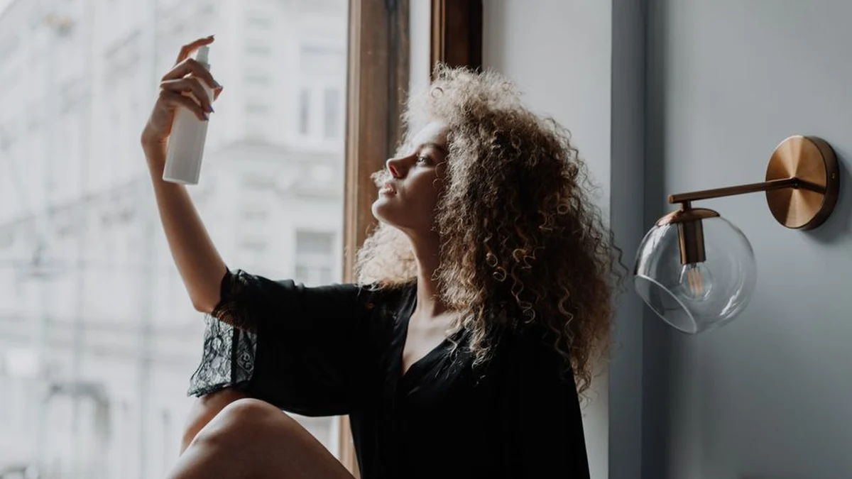 misting curly hair with a spray bottle by a window