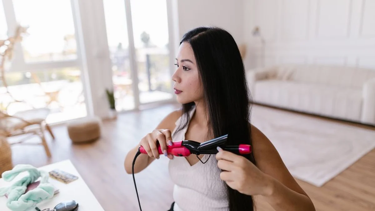 woman straightening her hair at home with a flat iron