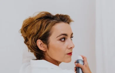 woman spraying her own hair with a finishing spray