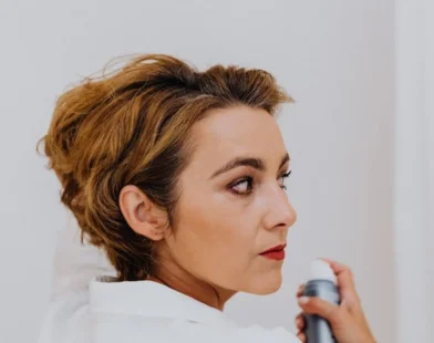 woman spraying her own hair with a finishing spray